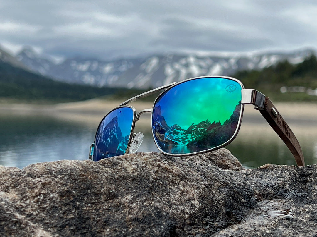 premium wooden sunglasses on a lake at glacier national park with blue lenses and mountains