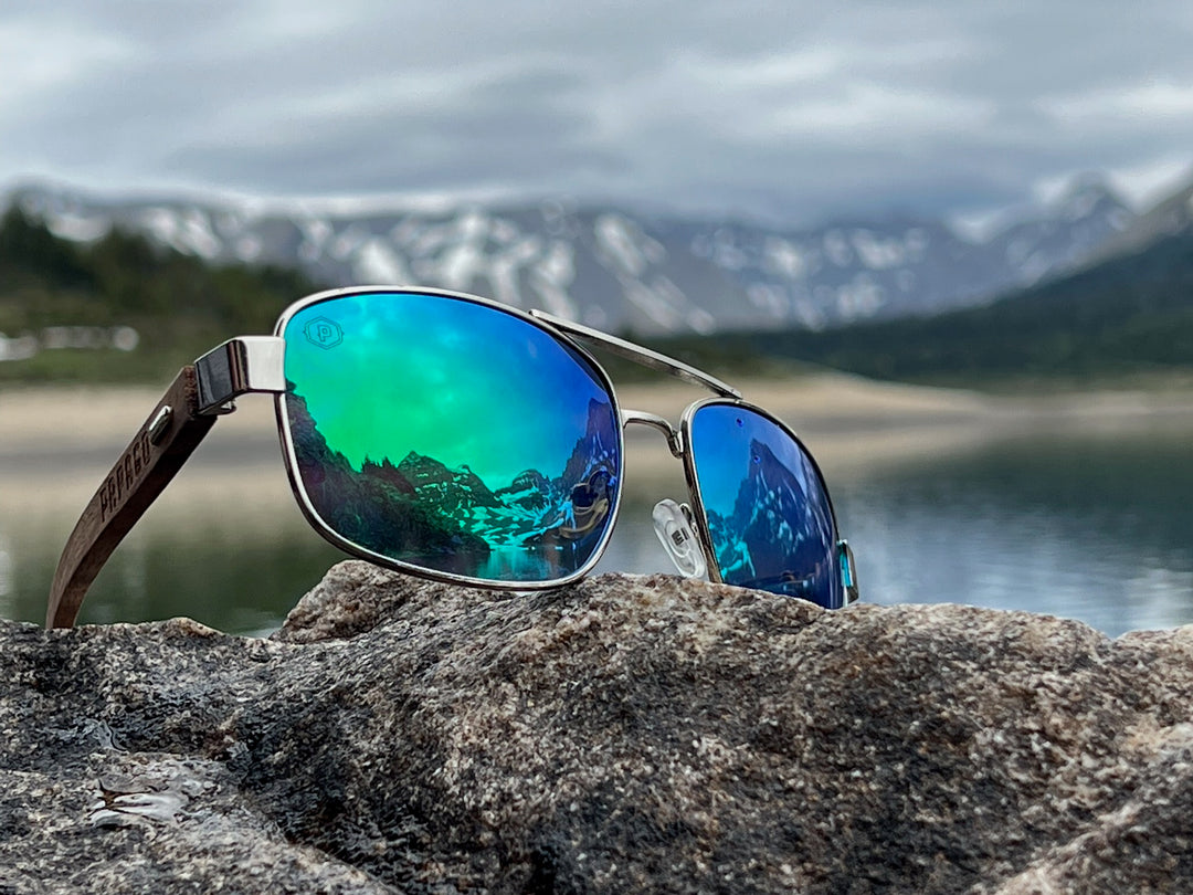 premium wooden sunglasses on a lake at glacier national park with blue lenses and mountains